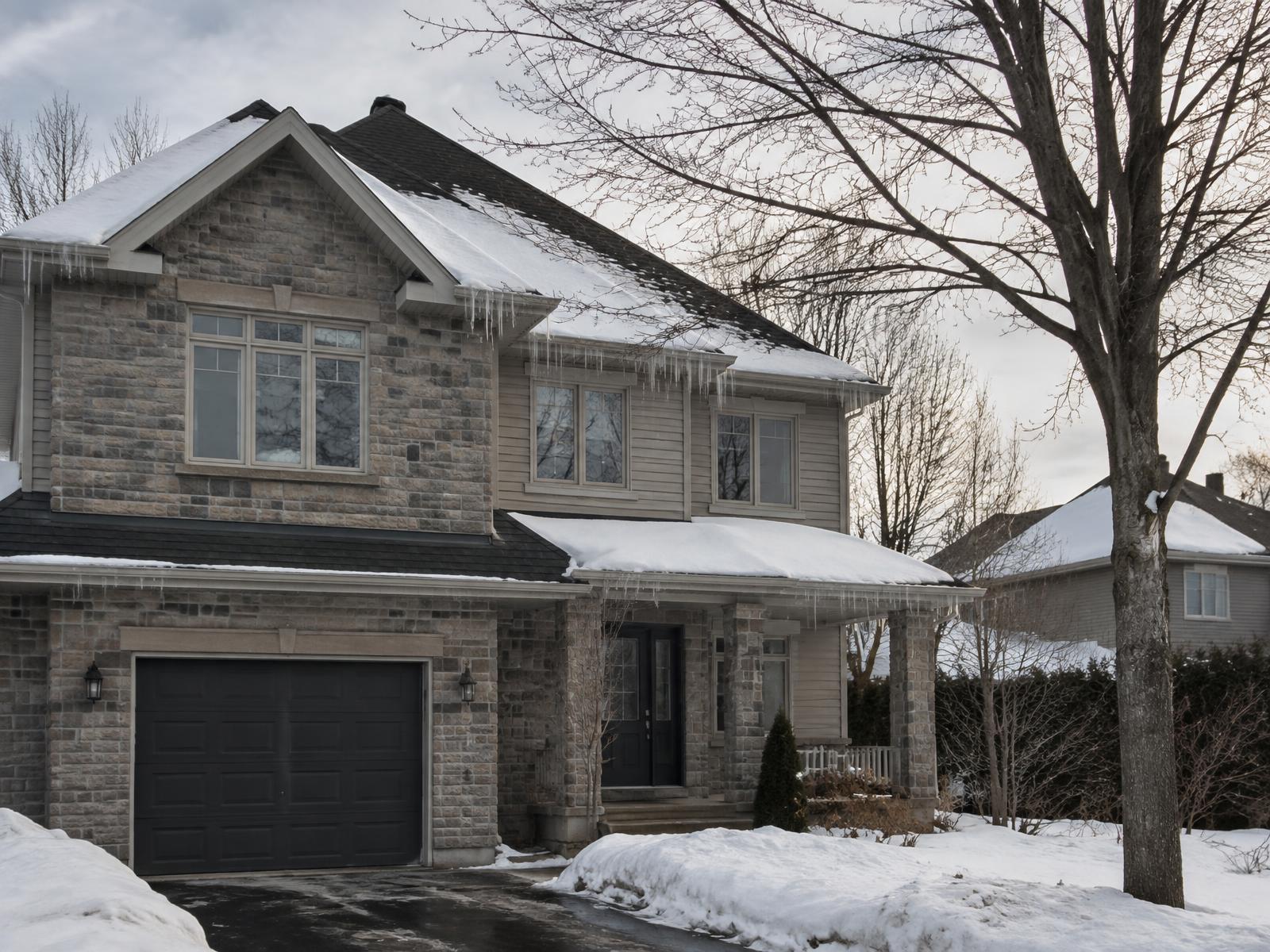 Maison résidentielle québécoise en hiver, neige sur la toiture de bardeau et glaçons aux avant-toits